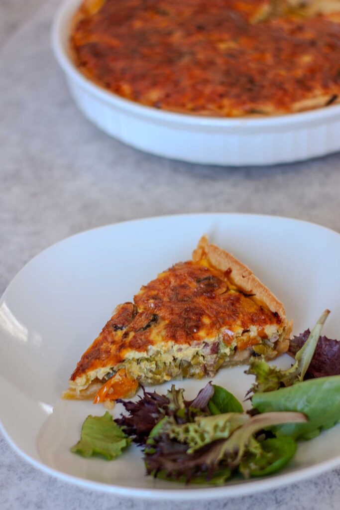 Een in een punt gesneden quiche met een goudbruin korstje op een rond bord met gemengde sla