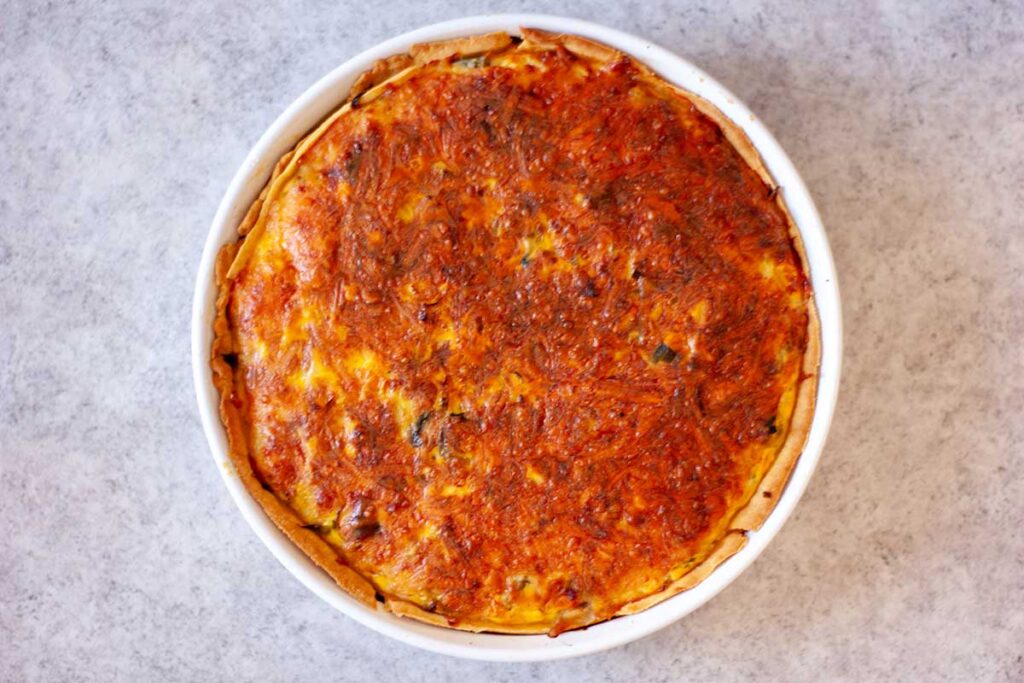 Quiche met een goudbruin korstje in een witte quichevorm