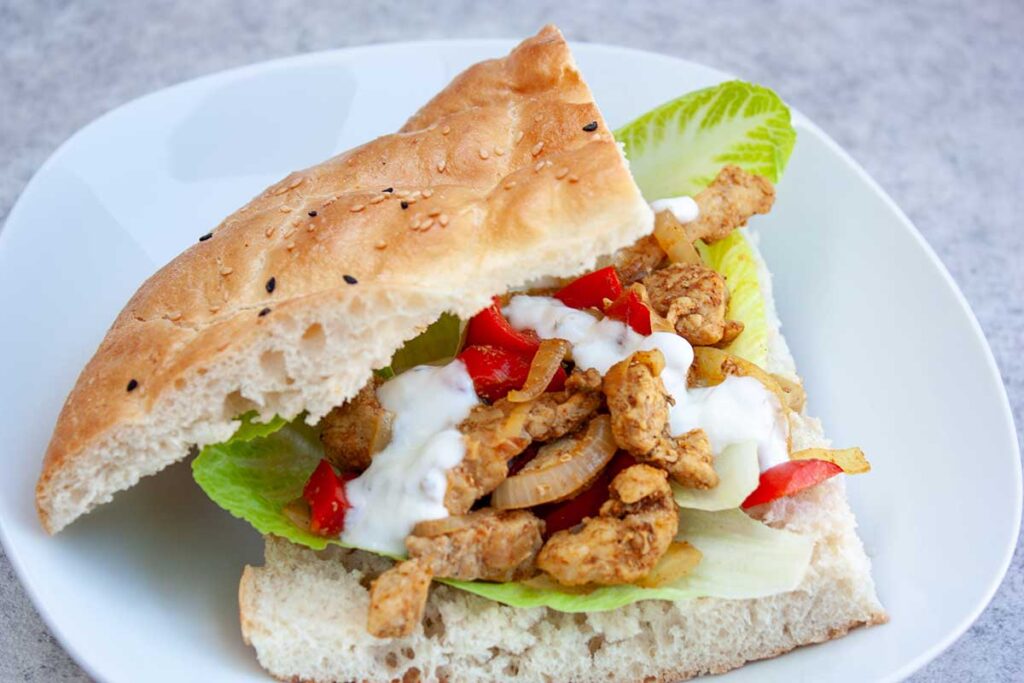 Bord met opengesneden Turks brood dat belegd is met shoarma, sla, komkommer en knoflooksaus