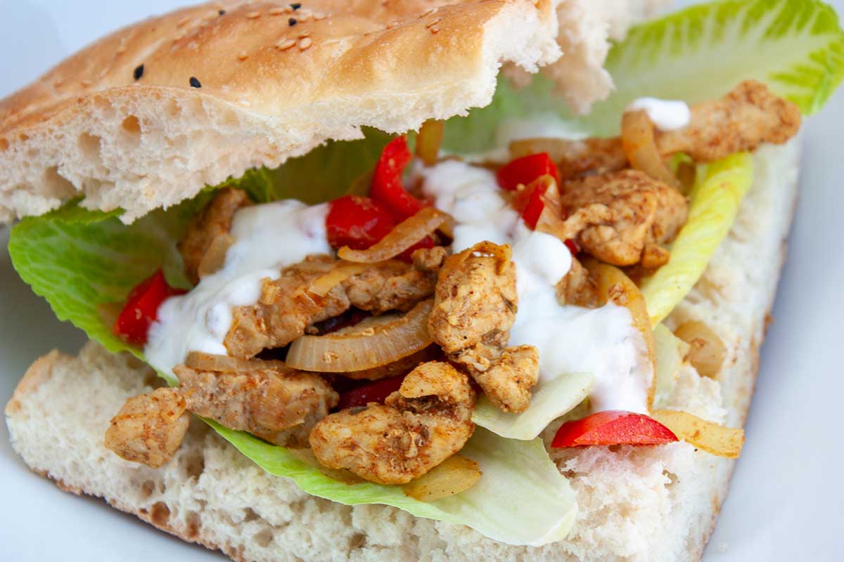 Bord met opengesneden Turks brood dat belegd is met shoarma, sla, komkommer en knoflooksaus