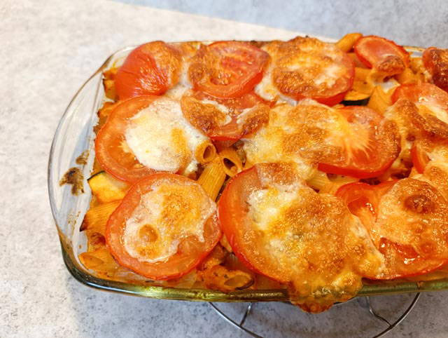 Ovenschaal met pasta ovenschotel bedekt met plakjes tomaat en gesmolten mozzarella