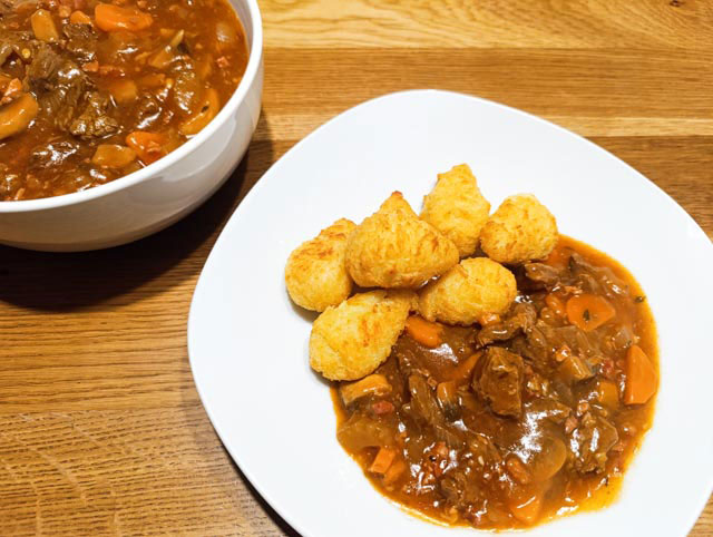 Wit bord met aardappelkroketten en boeuf bourguignon. Ernaast staat een witte kom met boeuf bourguignon