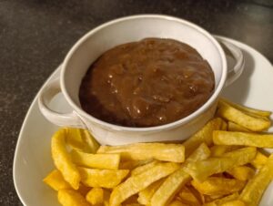 Witte kom met Limburgs zuurvlees. Ernaast liggen op een bord goudbruin gebakken frieten